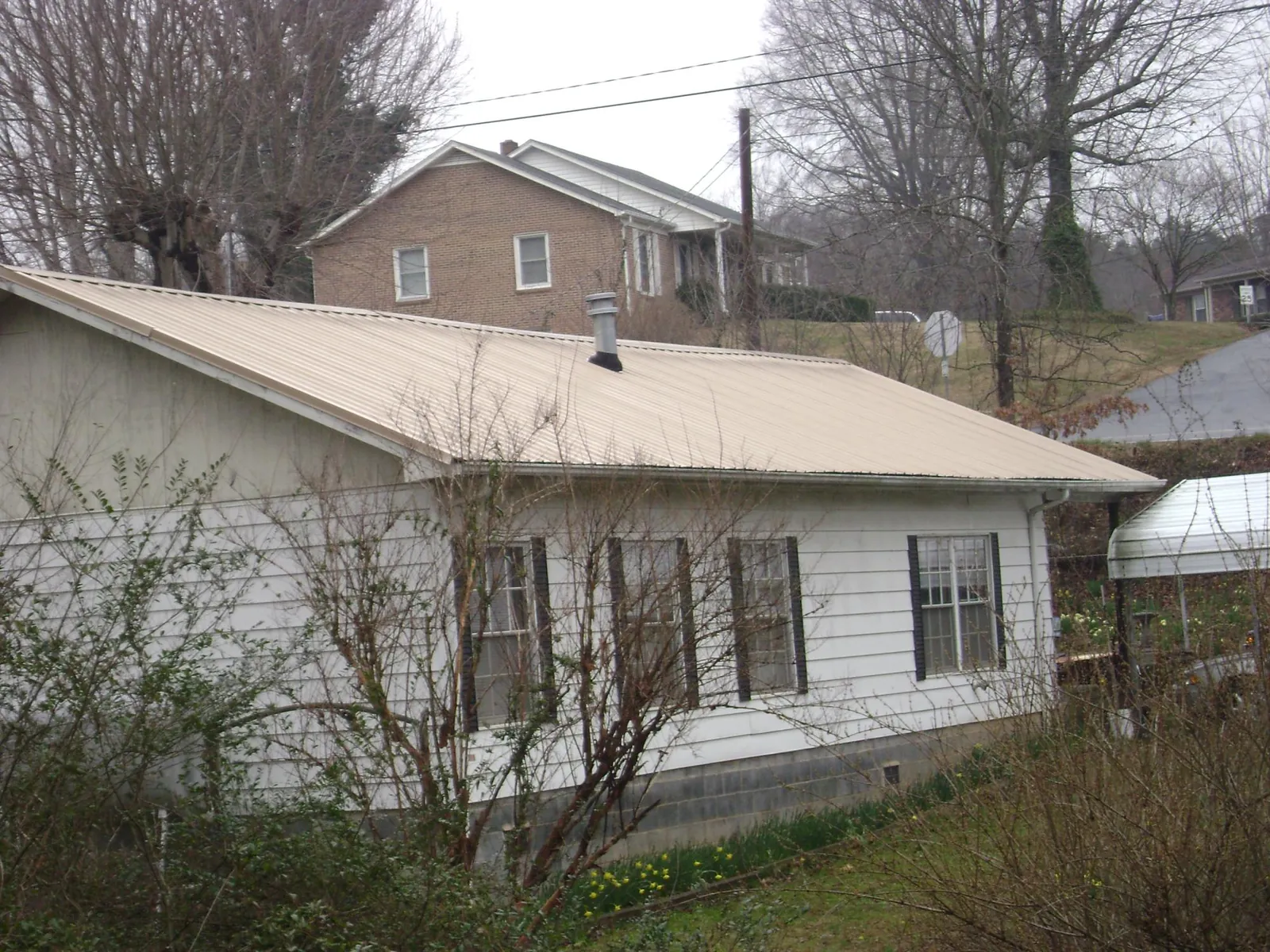 Tan metal roof on a white sided house set into a hillside — Commercial Roofing by Roofing Brothers in Kimberly